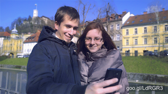  Attractive couple take a selfie photo while standing under Ljubljana castle in city center. Sunny day. Dressed in jacket.