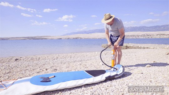 Wide shot dolly slide around a middle aged person in focus wearing a straw hat and concentrated on pumping the board.