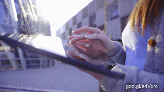 Female person using big screen tablet outside on a sunny day with business complex in background. Futuristic theme. Casual clothes. Polished nails. Jib shot.