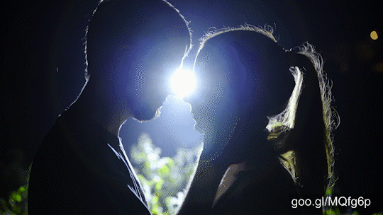 Two silhouette person at pitch black night kissing while a strong spotlight moon shining in the middle.